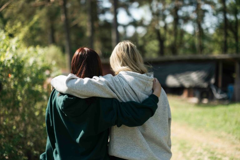 Kaksi hupparipukuista nuorta selin, pitävät toisiaan harteista. Kesäinen vuodenaika,